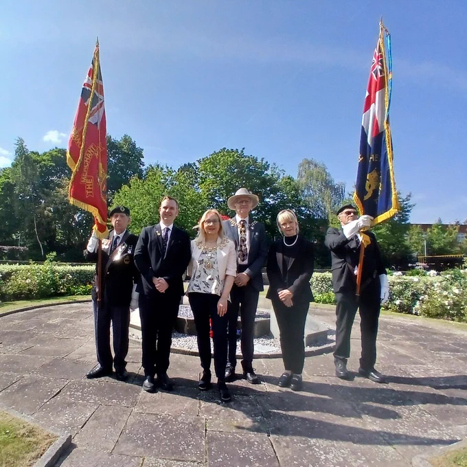 Leader of the Council Tom Ross, Mayor of Trafford Jane Brophy, mayoral consort John Brophy, and Trafford Chief Executive Sara Todd stand in the sunken garden at Trafford Town Hall, flanked by flag bearers, to celebrate the anniversary of VJ Day.