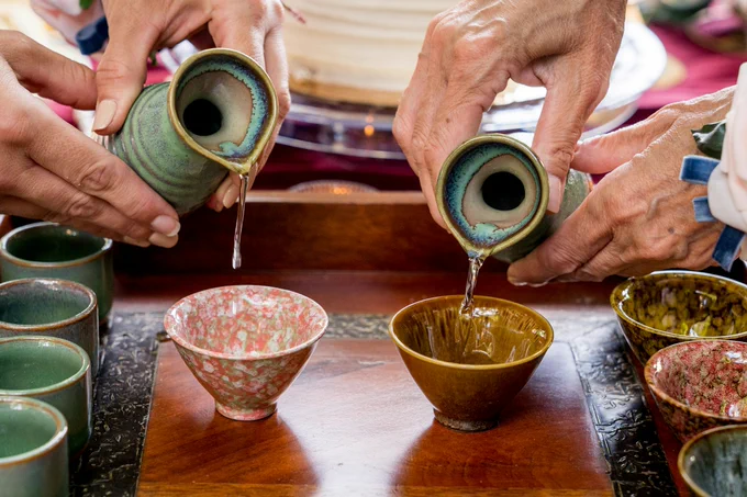 Photograph of Sake being poured into decorative wedding cups. By Frederick Shaw under a free Unsplash license: https://bit.ly/3IvgQFT
