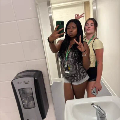 Two individuals taking a selfie in a restroom, with both flashing a peace sign.