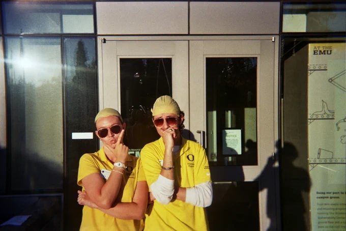 Two individuals in yellow uniforms making playful gestures in front of the EMU.