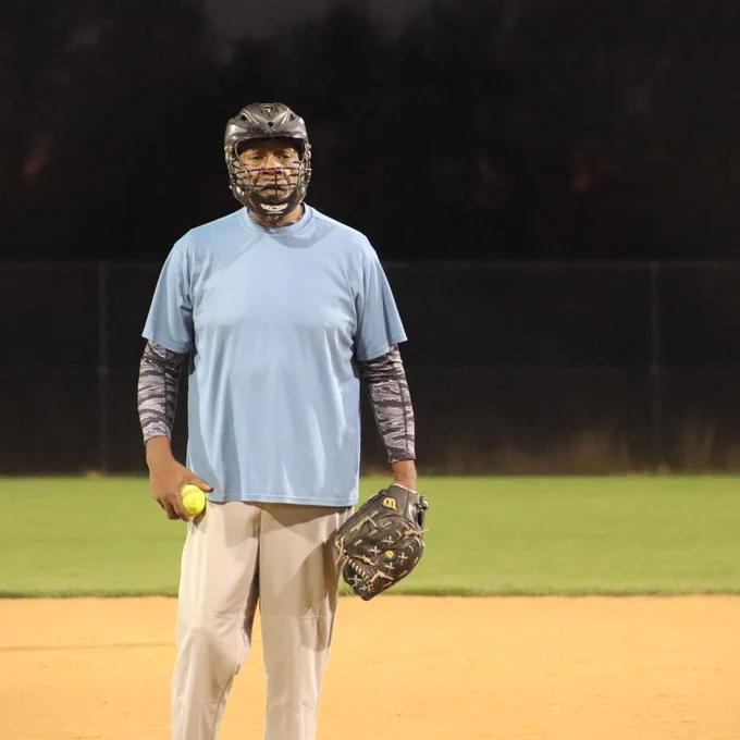 A man stands with a softball in one hand and glove in the other.