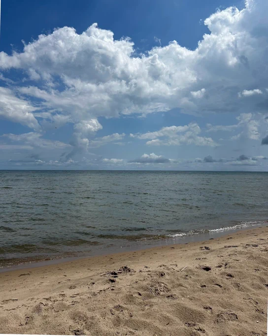 View of a tranquil beach with clear blue skies and fluffy clouds overhead, complemented by calm ocean waters and sandy shores.