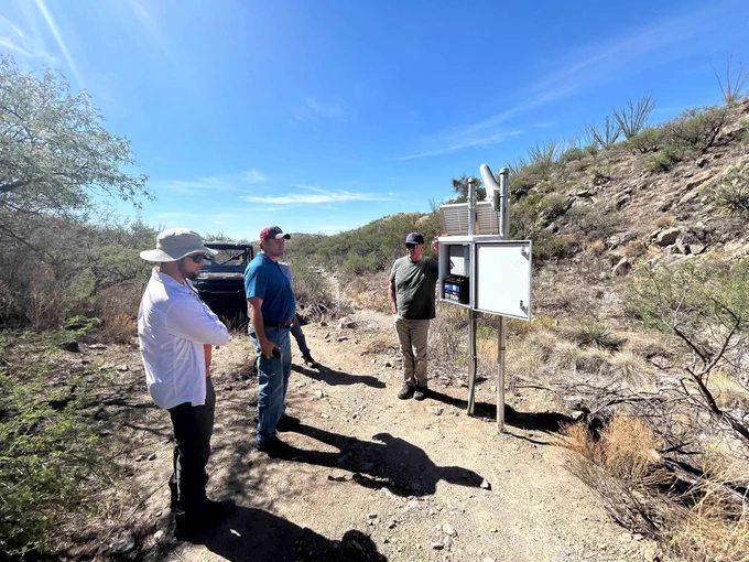 USGS scientists stand next to a newly installed stream gage system in an arid land stream channel.