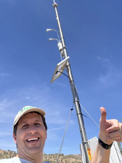 USGS scientist R. Petrakis gives a thumbs up and smiles taking a selfie with the evapotranspiration tower’s solar panel and LI-710 Evapotranspiration Sensor behind him. 