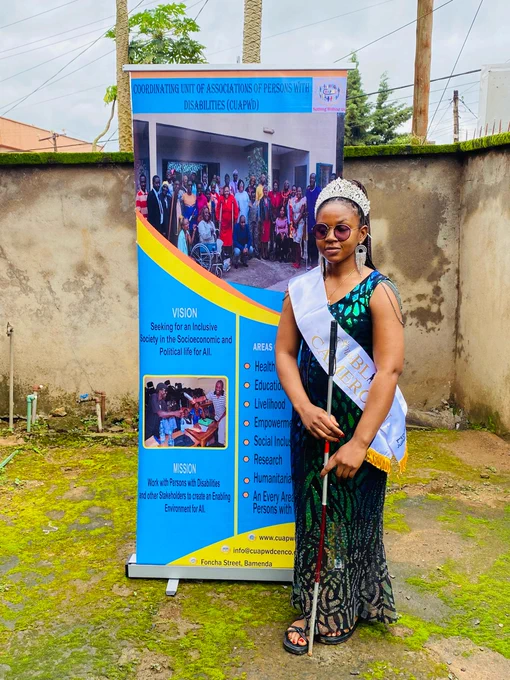 Louisa is standing in front of the Roll-up of CUAPWD while holding her white cane