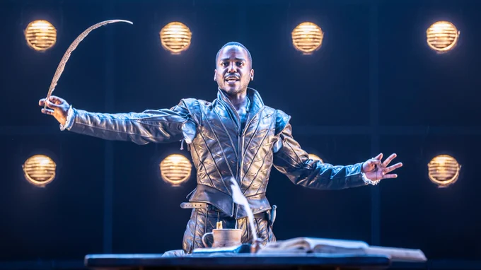Ncuti Gatwa, with his leather jerkin fully buttoned up, holding a tall quill to his side
