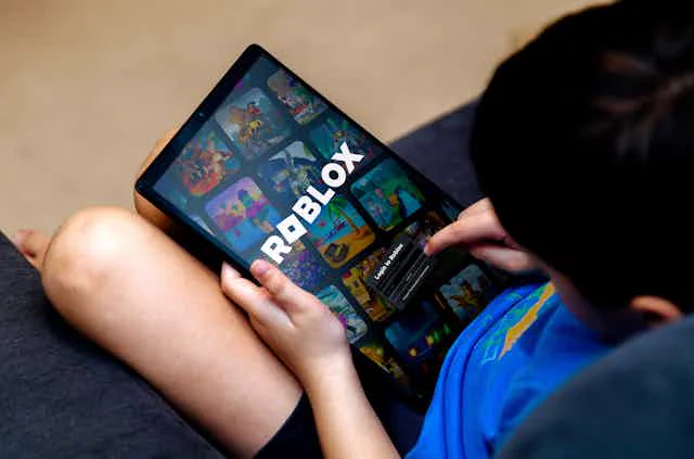 Ein Kind hält ein Tablet in der Hand, auf dem das Roblox Logo zu sehen ist 