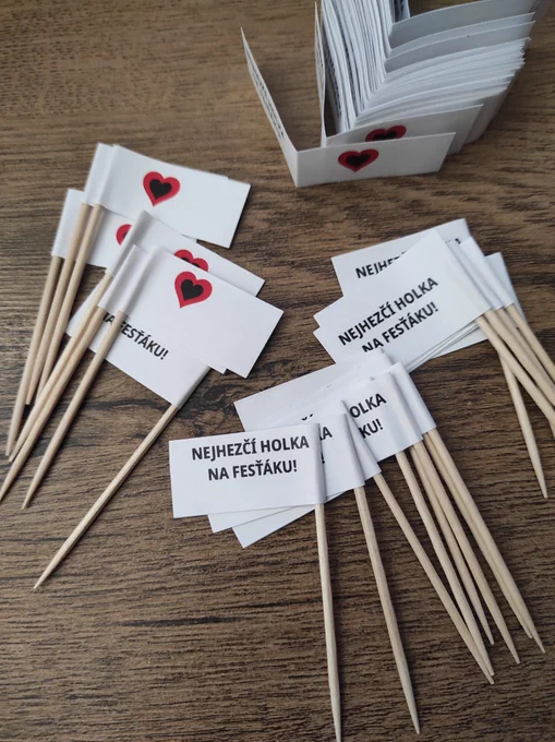 Ručně vyrobené vlaječky se srdcem na jedné straně a s textem „NEJHEZČÍ HOLKA NA FESŤÁKU!“ na druhé.