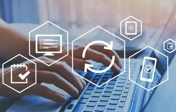 Hands typing on a laptop in the background with icons of a computer, phone and tablet in the foreground