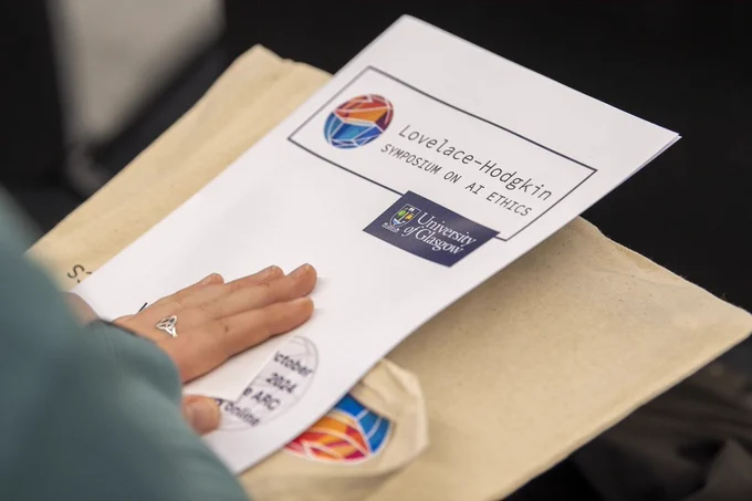 A photograph of a hand holding the programme for the 2024 Lovelace-Hodgkin Symposium