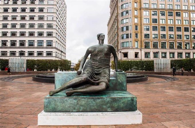 A large bronze sculpture by Henry Moore of a reclining woman, nicknamed 'Old Flo'. It is in an urban setting with high-rise buildings behind.