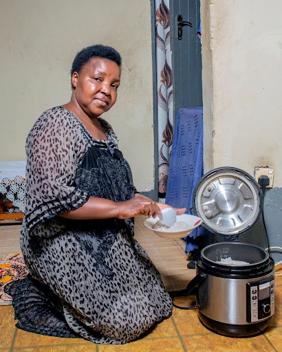 An African lady sitting down in a kitchen environment serving food from an Electric Pressure Cooker.