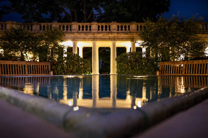 Evening view of a reflective pool at UVA featuring glowing lights and surrounded by benches and lush greenery.