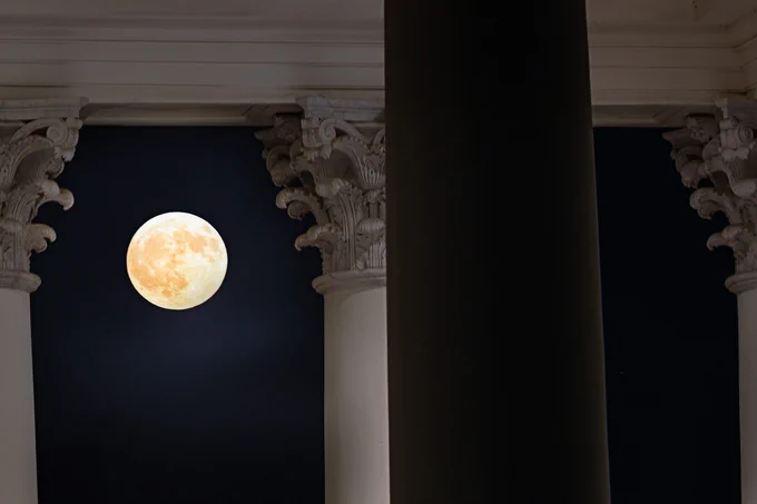 Full moon viewed between two classical columns in a dark night sky.