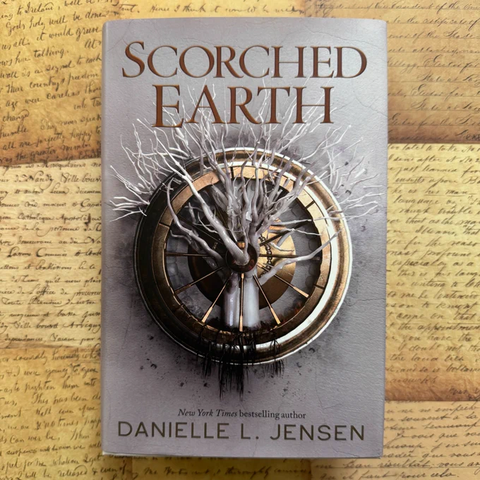 A copy of Scorched Earth by Danielle L. Jensen resting on a background made up of aged, hand-writtten letters.