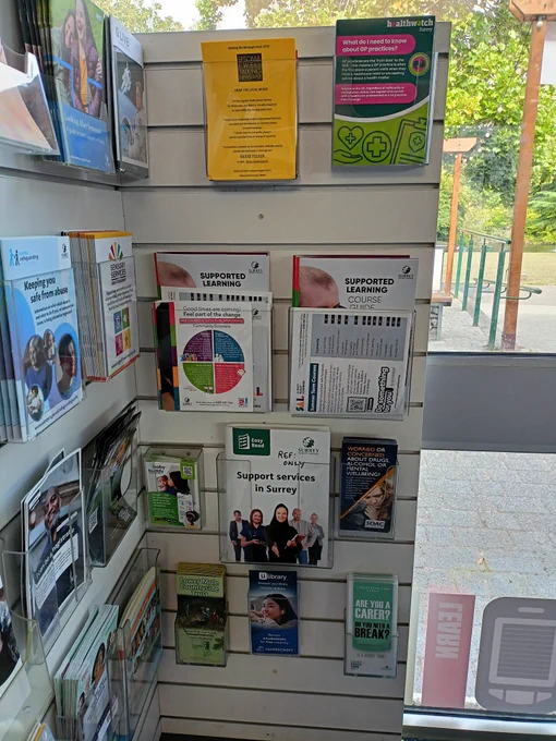 Photograph of a stand displaying information leaflets in plastic holders. The leaflets include information on Support Services in Surrey, Supported Leaning Courses, and Healthwatch Surrey.
