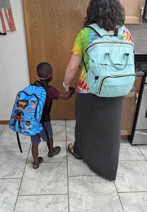 A mother and son walking out the door wearing backpacks 
