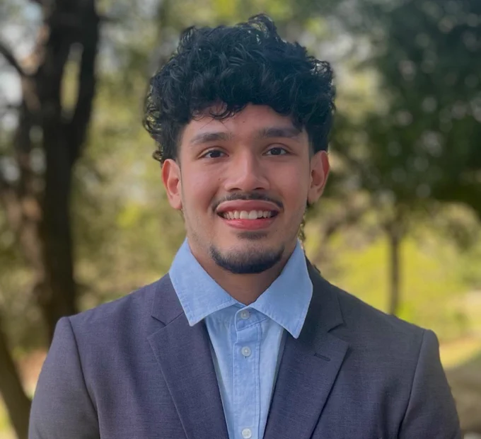 Person in a blue suit smiling at the camera with a natural outdoor background.