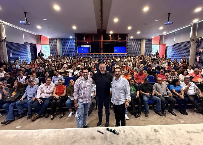 Three people stand in front of a large auditorium full of seated people.