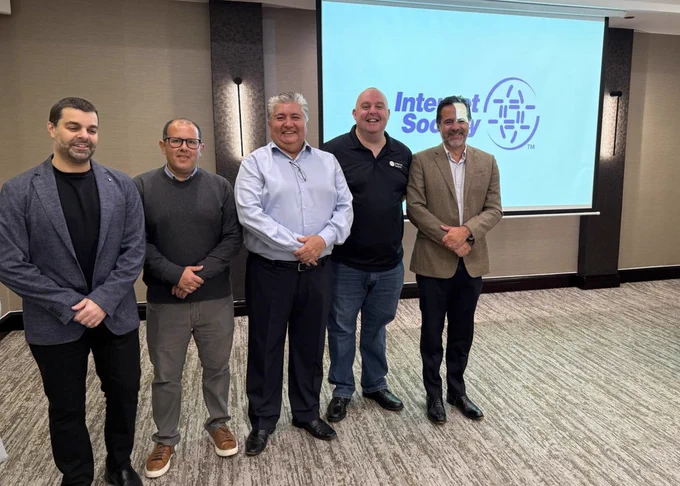 Five people stand in front of a projection screen showing an older Internet Society logo.