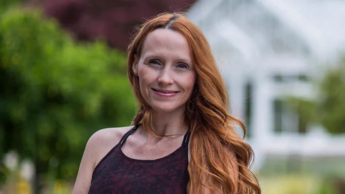 Dr. Melissa Perreault poses for a portrait with green trees and a white building blurred in the background.