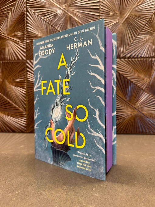 A copy of A Fate So Cold by Amanda Foody and C.L. Herman with purple sprayed edges in front of a bronze patterned background.