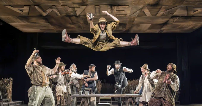 A performer jumps off a table and is surrounded by other performers who are cheering. 