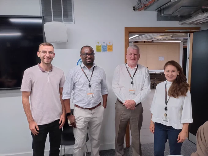 Four staff members stand smiling in an office environment.