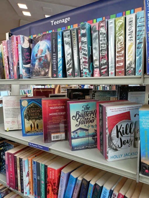 Photograph of a shelf of books with the books angled with the covers facing outwards. Book titles include Kill Joy by Holly Jackson, The Butterfly Tattoo by Phillip Pullman, and As Long As the Lemon Trees Grow by Zoulfa Katouh.