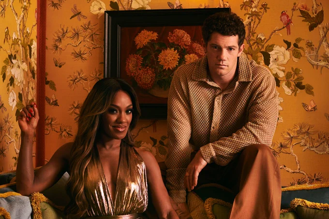 A photo showing two individuals in suave outfits posing in an ornate, rustic room 