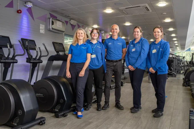 5 people dressed in blue standing in a gym space
