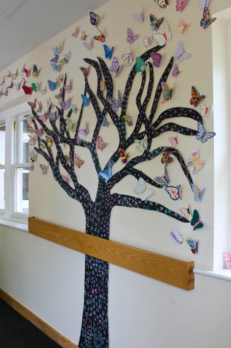 Full length photo of tree made from card. The bark of the tree has forget me not flowers painted onto it, and there are lots of butterflies made from card which are all painted different colours.
