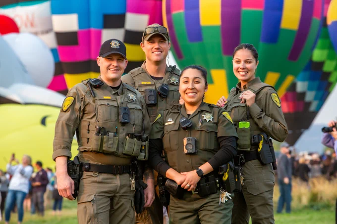 4 deputies standing in front of hot air balloons, smiling at the camera
