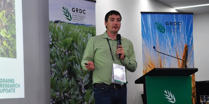 Dr Joshua Fanning speaking into a microphone and standing in front of GRDC banners. 