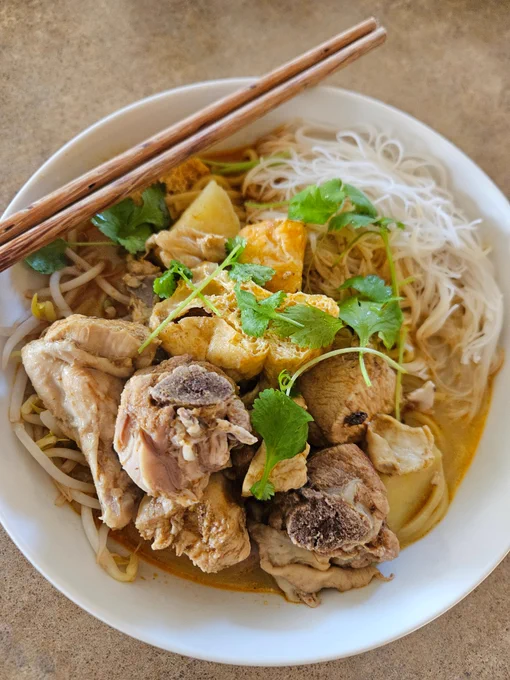 Dinner as described served in a round white bowl. A pair wooden chopsticks lie on a diagonal atop the bowl.