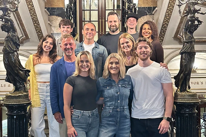 A photo showing a group of individuals smiling together in a theatre foyer 