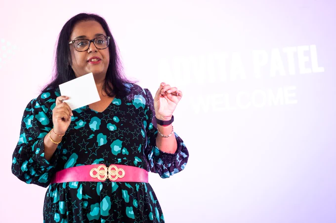 This image shows Advita holding a card and speaking at an event.