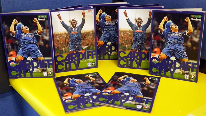 Signed copies of the official Cardiff City matchday programme, laid out on a yellow bench in the away dressing room at CCS.