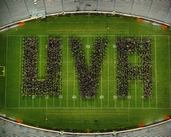 Aerial view of a large group of people forming the letters "UVA" on a football field, representing the University of Virginia.