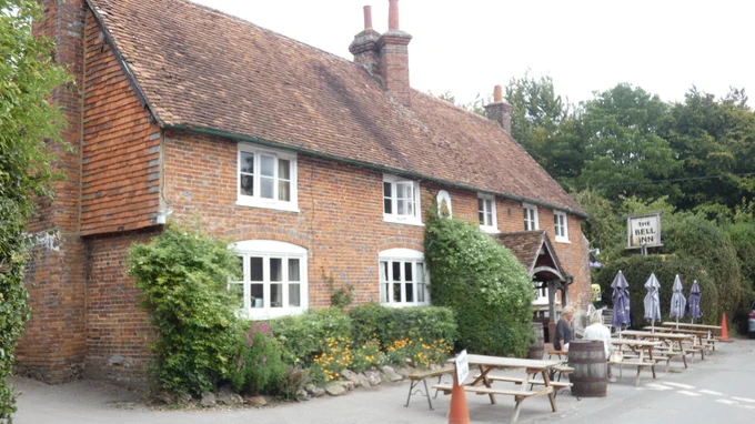 Photo by Richard Marshall. Exterior of pub with bench seating sets on roadway in front of pub.