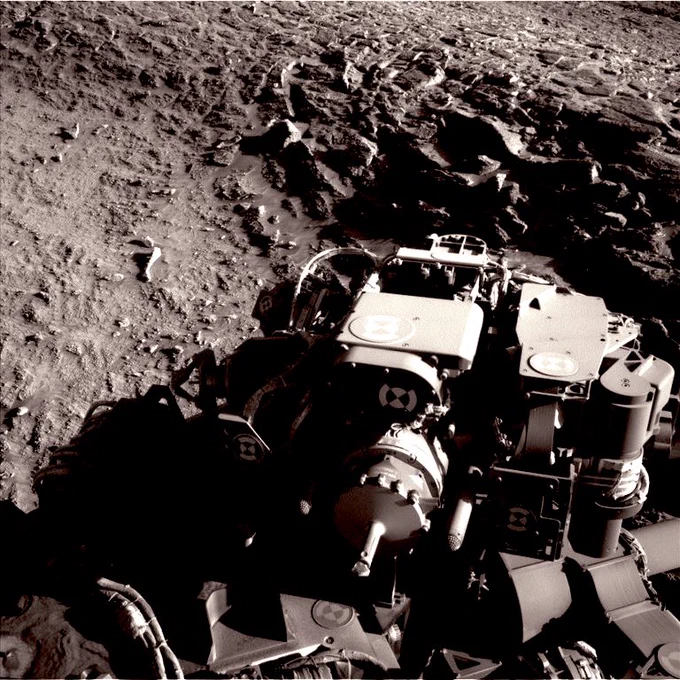 NASA’s Curiosity rover positioned at the base of the Río Frío fracture wall on Mars, captured by Left Navigation Camera in grayscale, showing a rugged, nodule-strewn ridge rising against the hilly Martian regolith under a flat sky, with scattered rock fragments. Image courtesy by NASA