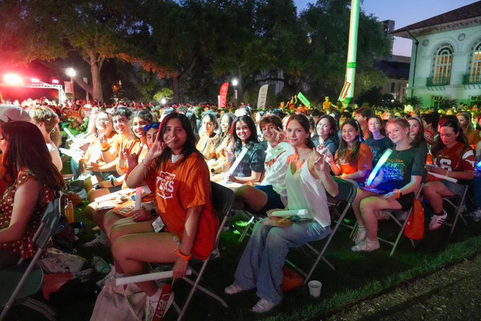 Outdoor gathering of University of Texas students wearing school colors and enjoying an event at night.