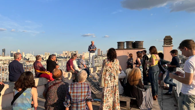 A crowd watches poet Jason Stoneking reading from his Sky Sketches series on a rooftop in Paris