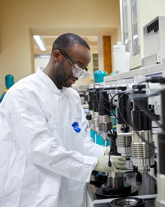 Person in a lab coat and safety goggles working with scientific equipment in a laboratory.