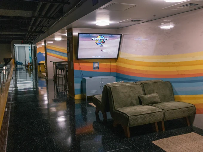 A casual lounge area at Tulane University featuring a sofa, a rug, a wall-mounted television displaying content, and a striped wall in colorful bright hues.