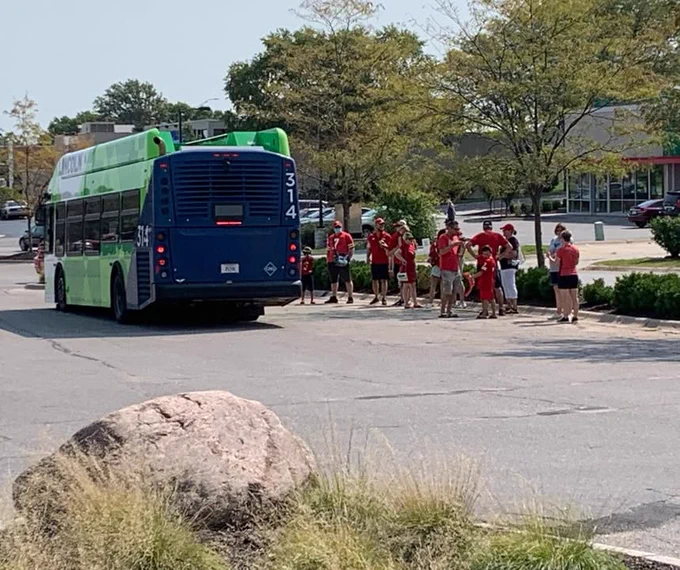 A group of Nebraska football fans in red shirts waiting to board a StarTran bus in a parking lot on a football game day.