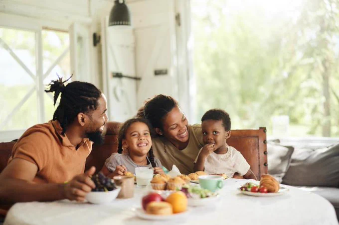A family of four enjoying a meal together at a dining table inside a bright, airy room.