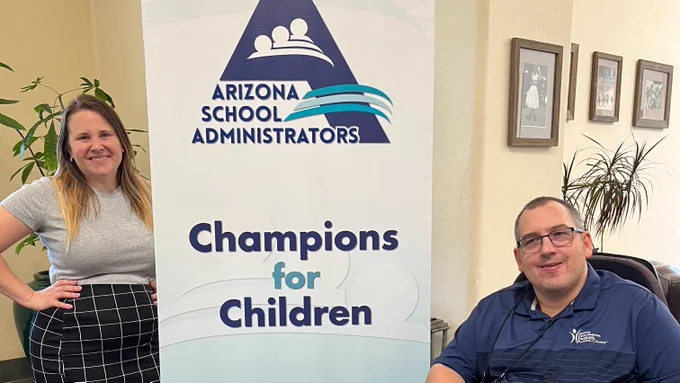 A man and a woman smile on either side of a banner reading, "Arizona School Administrators Champions for Children"