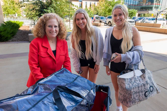 Chancellor Jennifer Mnookin poses for a photo with twin UW–Madison students in front of their red move-in cart.