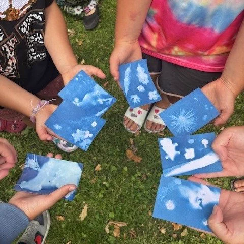 Children stand in a circle holding solar powered prints made with cyanotype paper
